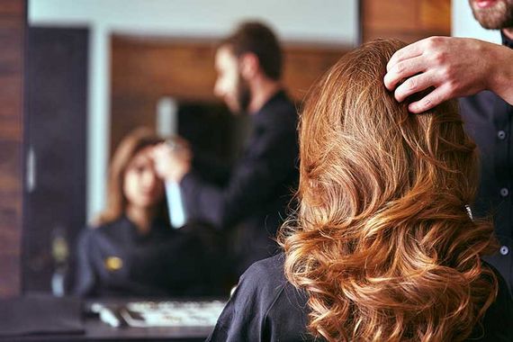 Friseurin stylt einer Kundin die Haare, während die Frau mit glänzenden Locken in den Spiegel schaut