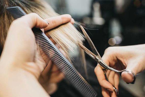 Friseur schneidet blondes Haar mit einer Schere, während er eine Strähne mit einem Kamm hält