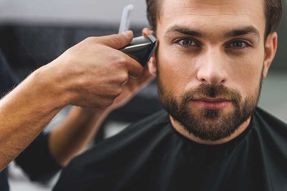 Friseur trimmt die Seiten eines bärtigen Mannes mit einer Haarschneidemaschine