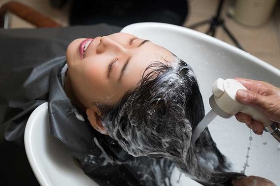 Kundin lehnt entspannt im Friseursalon zurück, während ihr die Haare im Waschbecken shampooniert werden