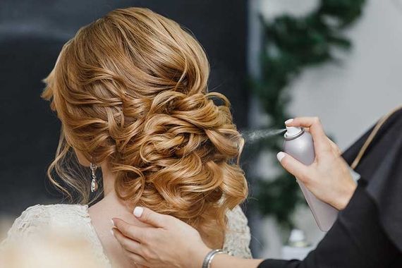 Friseurin fixiert eine elegante Hochsteckfrisur einer Kundin mit Haarspray